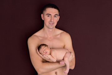 Naklejka premium Newborn 5 day naked boy, lies in his father's arms and sleeps. Happy young dad with a naked torso holds a newborn son in his arms.