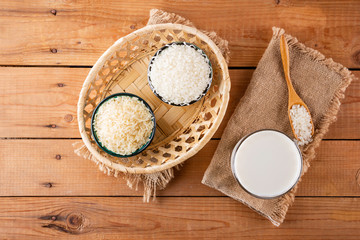 Rice milk and rice seeds on wooden boards. Rice milk in glass on sackcloth. Vegan non-dairy milk on wooden background. Alternative milk from rise. Rustic style. Top view