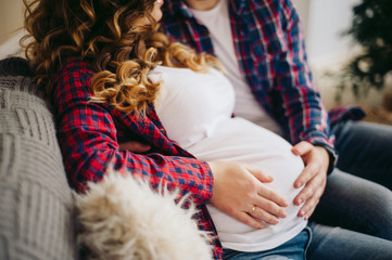 pregnant young woman sits next to her man, both hold hands on her belly