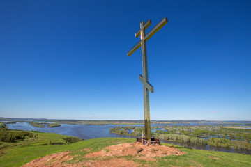 Orthodox worship cross on a hilltop on the high bank of the Kama River on the background of the river and meadows, on a sunny summer day