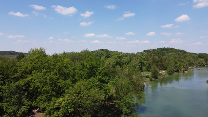 drone shot over lake with green trees and blue sky