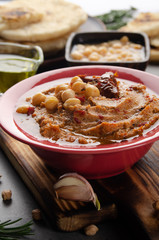 Fresh homemade Hummus in clay dish topped with olive oil, chickpeas, spices and sun dried tomatoes on stone table