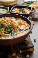 Fresh homemade Hummus in clay dish topped with olive oil, chickpeas and chopped green coriander leaves on stone table served with spices