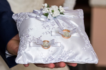 The groom holds a white pillow with wedding rings