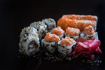 Delicious rolls and red pickled ginger versus black background. Rolls with fish and rice