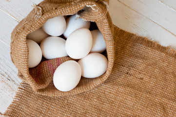 White chicken eggs lying in a canvas bag, shot on a white painted wooden surface. Background for...