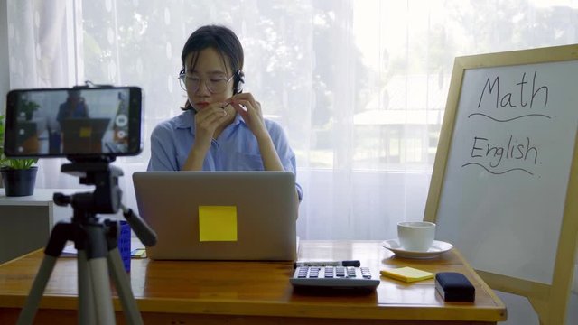 An Asian woman is teaching online via a laptop via webcam.