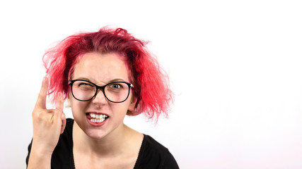 A girl rocker with red hair and glasses squinting one eye shows a hand gesture Heavy Metal HM on a white background. Concept of informal youth and heavy rock.