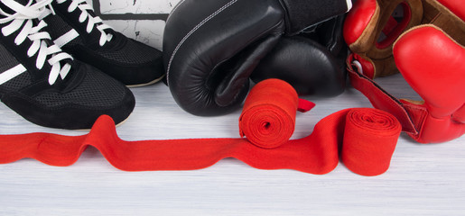 red bandages for fixing joints, sneakers, a protective helmet and boxing gloves, against a light brick wall, close-up
