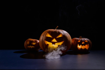 Halloween card. jack o lantern with candles glow on a black background. A row of creepy pumpkins with carved grimaces smokes in the dark.