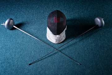 Two swords and mask lie on a blue background. The concept of fencing.