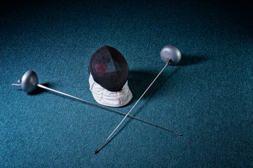 Two swords and mask lie on a blue background. The concept of fencing.