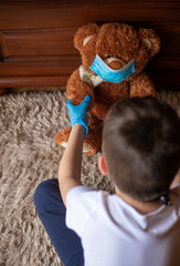 Little boy holding a teddy bear in mask and gloves