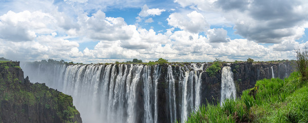 Panorama view of Victoria Falls of Zambezi River, border of Zambia and Zimbabwe with blue sky and dramatic clouds - obrazy, fototapety, plakaty