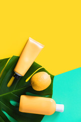 Summer bright yellow blue flatlay on colorful background with tubes with sunscreen, lemon and leaf of monstera. Hard shadows and light. Top view. Flat lay. Trend style. Copyspace.