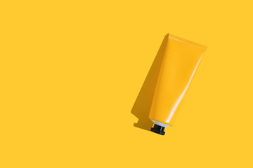 Yellow tube of sunscreen on a bright yellow background with hard shadow. Sun protection in the summer.