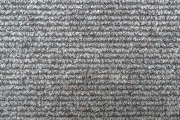A fragment of a woolly shaggy woven doormat made of alternating light gray and dark gray stripes woven in frequent thick loops. Textile canvas background.