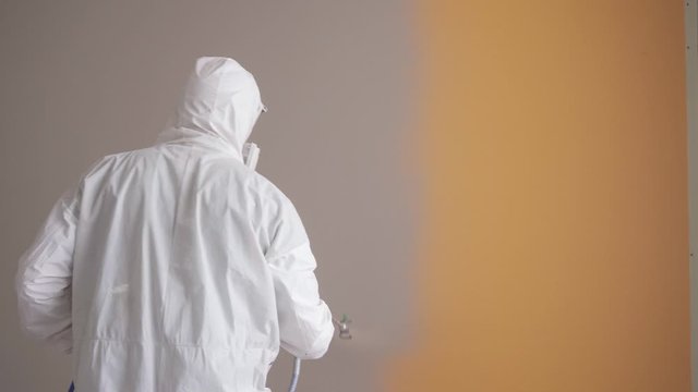 Airless Spray Painting. Worker painting the orange wall by airless spray gun with white color