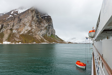 Obraz premium Lowering orange lifeboat to water in Arctic waters, Svalbard. Abandon ship drill. Lifeboat training. Man over board drill.