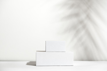 Fototapeta premium White empty stands on light shadow background. Blank unbranded shopfront. Showcase for cosmetic products. Product advertisement. Copy space. Cosmetology and beauty concept