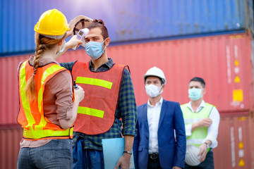 Technician or engineer worker use infrared thermometer measure temperature of other staff in shipping container workplace area and they stay in line during covid pandemic in around the world.