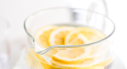 A close up view of a pitcher of lemon water with lemon slices in soft focus.