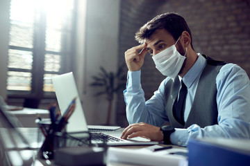 Obraz premium Pensive businessman with face mask working on laptop in the office.