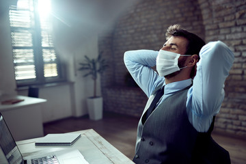 Relaxed businessman with protective face mask taking a break in the office.