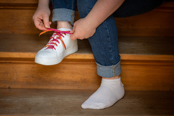 Junge Frau sitzt auf einer Treppenstufe und bindet einen bunten Schnürsenkel an weißem Schuh zu....