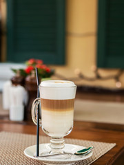 Morning at the cafe. A Cup of latte. Transparent glass. Several different layers of milk and coffee are visible in the glass. It's Sunny and warm outside. The atmosphere of an Italian restaurant or ca