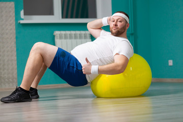 Overweight man is lying on a fitness ball during group fitness classes. Fat man looks satisfied with his result of weight loss trainings
