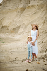 Funny girl 7 years old in jeans overalls and a hat with a blonde mom walking along the sandy beach and hugging