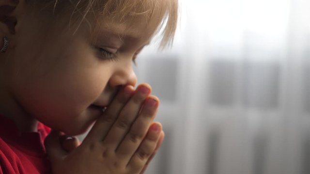 little daughter girl makes a wish prayers bedtime religion concept . prayer child indoors praying lifestyle by bed front of window