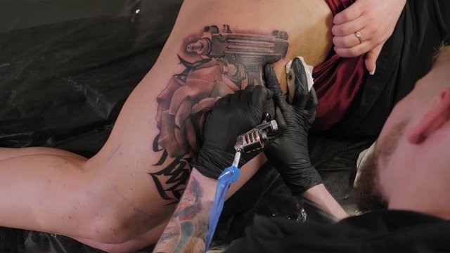 Close-up of a man with black gloves doing a tattoo on the leg of a young girl. Close-up of a needle with ink in the hand of a professional tattoo artist. Professional artist making tattoo in salon