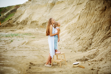 Funny girl 7 years old in jeans overalls and a hat with a blonde mom walking along the sandy beach and hugging