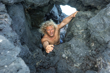 A young climber with long white hair climbs a rock against the background of the ocean
