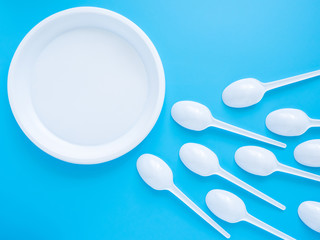 White plastic plate and spoon on a blue background. Conception of fertilization, pregnancy and contraception. The struggle of spermatozoa for an egg. Modern problems of conception and infertility