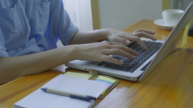 An Asian woman is teaching online via a laptop via webcam.