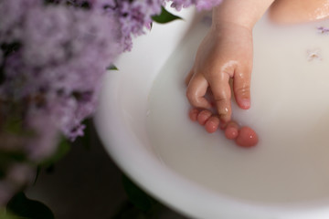 a child with a pen touches the toes of a foot in the water. bath with milk
