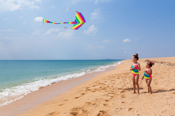 two little baby girls have fun on the beach on a summer Sunny day. Child playing with a kite while running outdoors. family vacation concept

