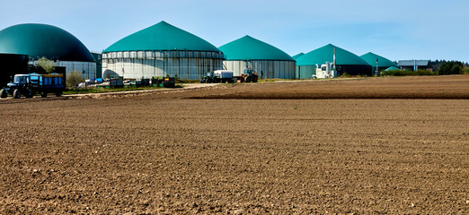 Brown withered field in front of a large plant for energy production from biogas produced in green...
