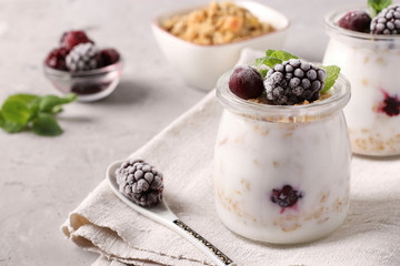 Fototapeta na wymiar Granola crispy honey muesli with natural yogurt, frozen berries and mint in glass jars on a gray background, healthy food