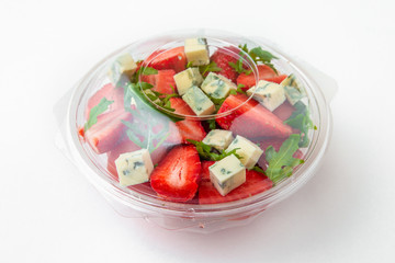 Salad in plastic package for take away or food delivery isolated on a white background. Nutritional Diet Snack with strawberries, dorblu cheese and arugula.