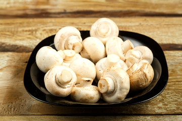 Fresh champignon mushrooms in a black plate on a wooden table.