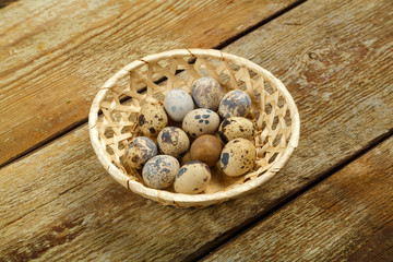 Fresh quail eggs in a wicker basket on a wooden table.