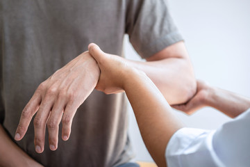 Doctor or Physiotherapist working examining treating injured arm of athlete male patient, stretching and exercise, Doing the Rehabilitation therapy pain in clinic