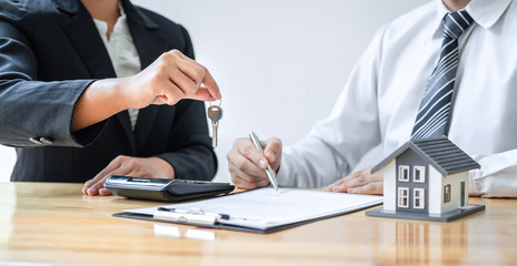 Home Insurance and Real estate investment concept, Sale agent giving house key to new client after signing agreement contract with approved property application form