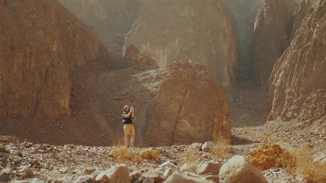 Tourist woman walk along the rock canyon and take photo in hot desert. Desert canyon background, Egypt, Sinai, 4k