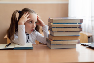 Girl sitting at a desk. The student looks at a stack of books. Tired at the desk. Study.