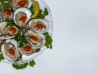 Serving of Apalachicola oysters with cocktail sauce and lemon on a glass plate garnished with green curly parsley and an offset white background.